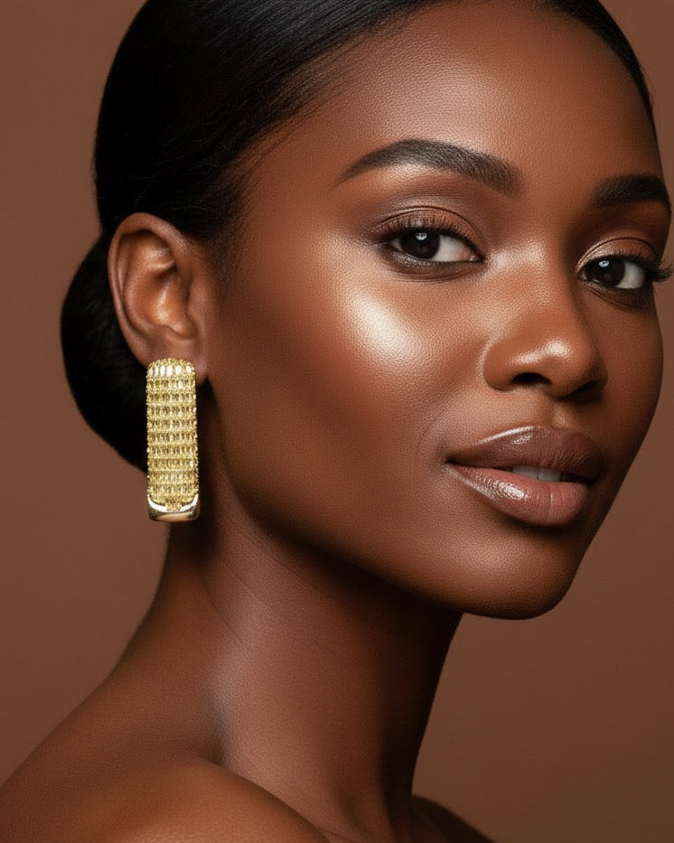 Close-up of a dark-skinned model wearing the Trinity Hoop Earrings. These large, high-fashion gold hoops catch the light, perfect for an editorial jewelry look that celebrates self-worth